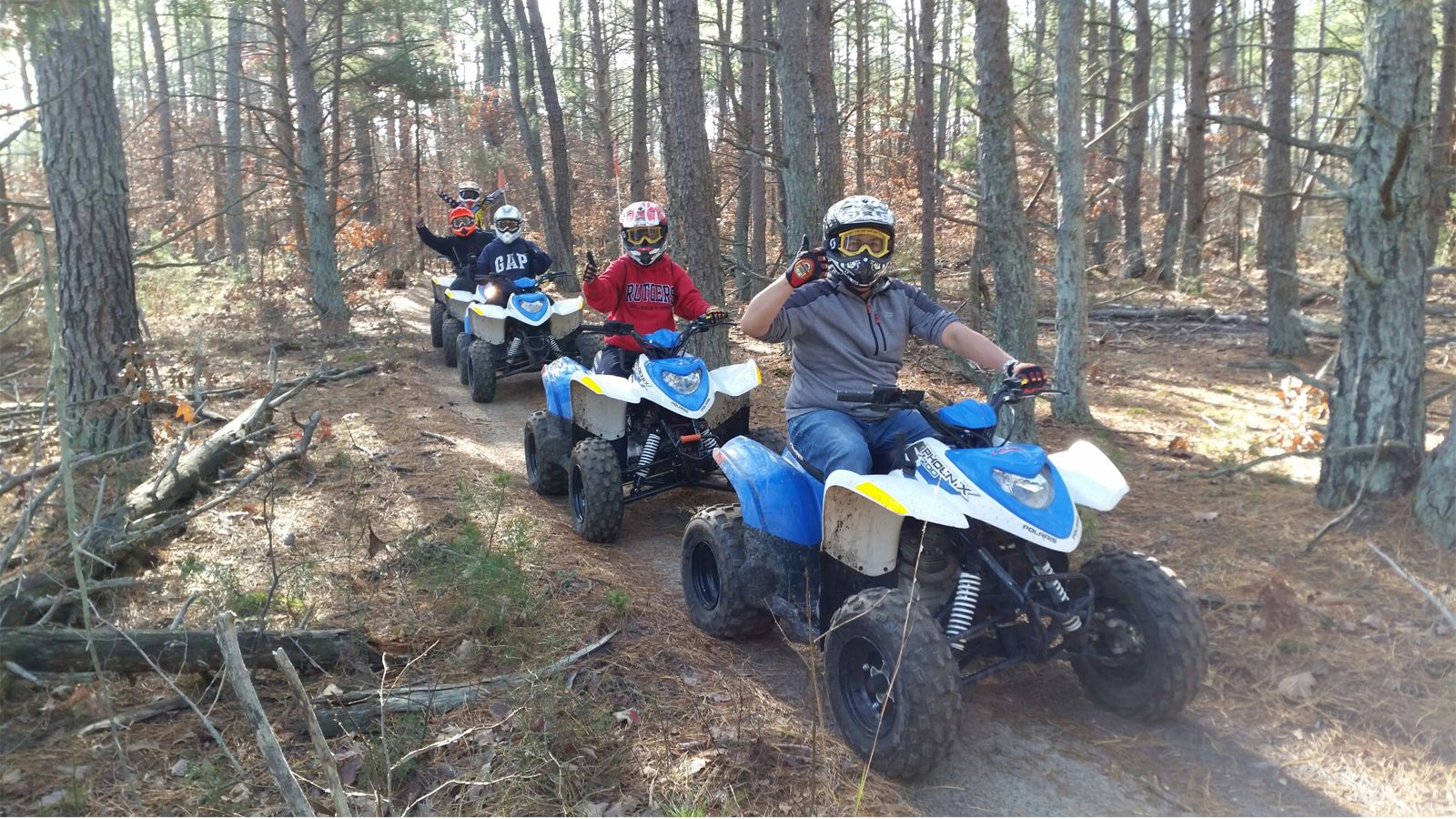 Group of riders on blue ATVs on a pine trail