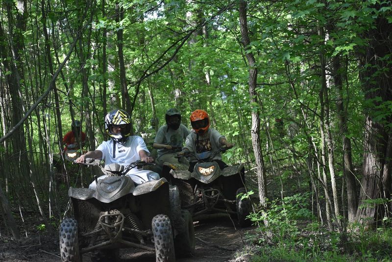 Riders in helmets following each other down a shaded wooded trail