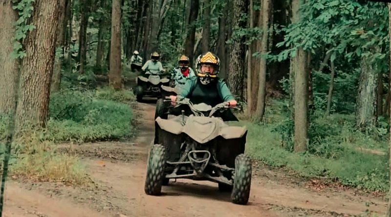 Line of riders in yellow helmets cruising a forest trail